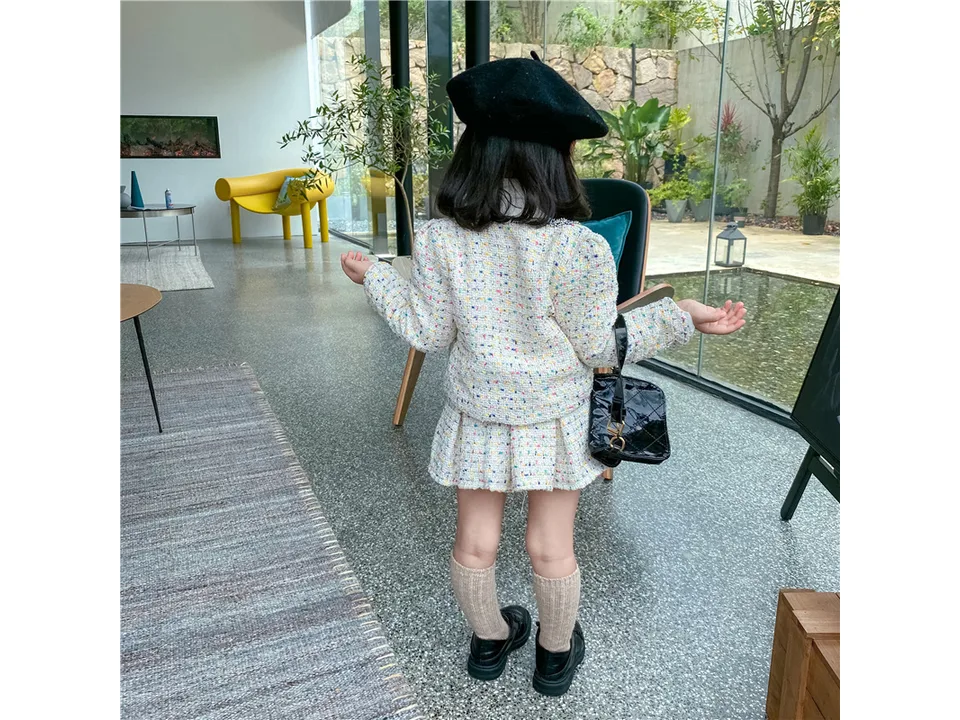 Back view of a young girl wearing a tweed jacket and pleated skirt set.