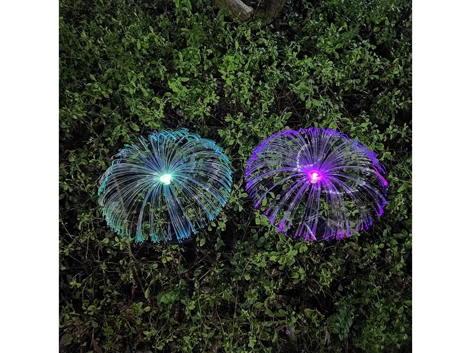 Two solar jellyfish lights in teal and purple glowing on the grass.