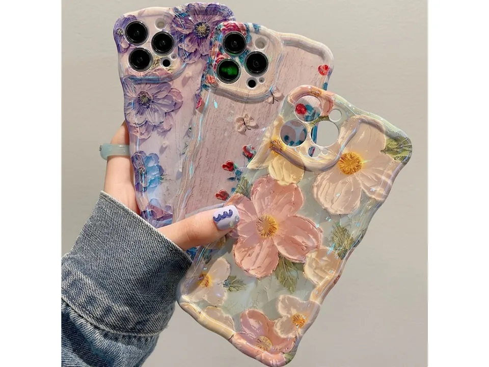 Three different floral oil painting style phone cases held in a hand.