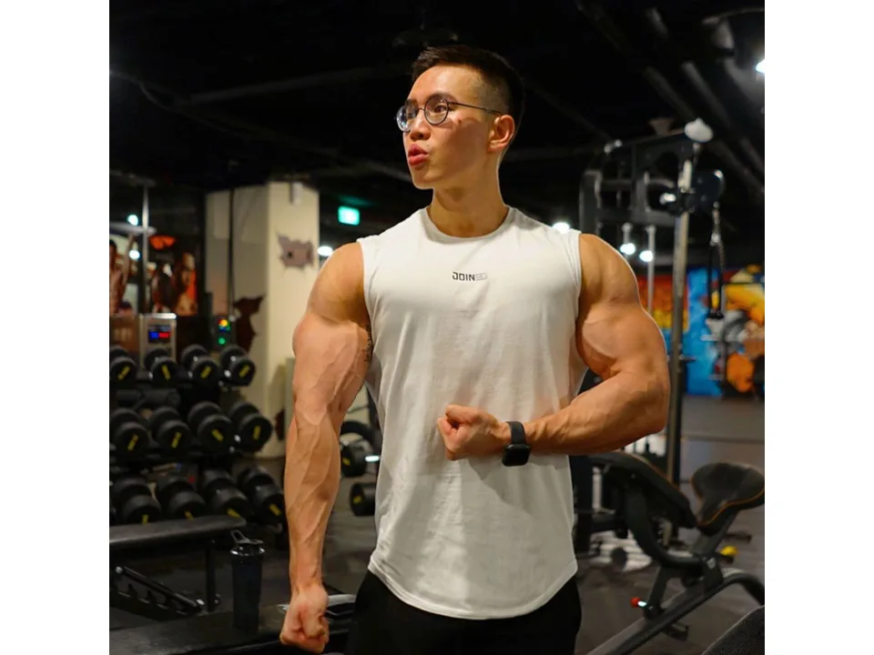 A man wearing a white sleeveless tank top in a gym.