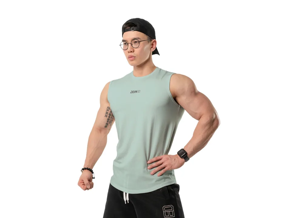 A man wearing a light green sleeveless tank top against a plain background.