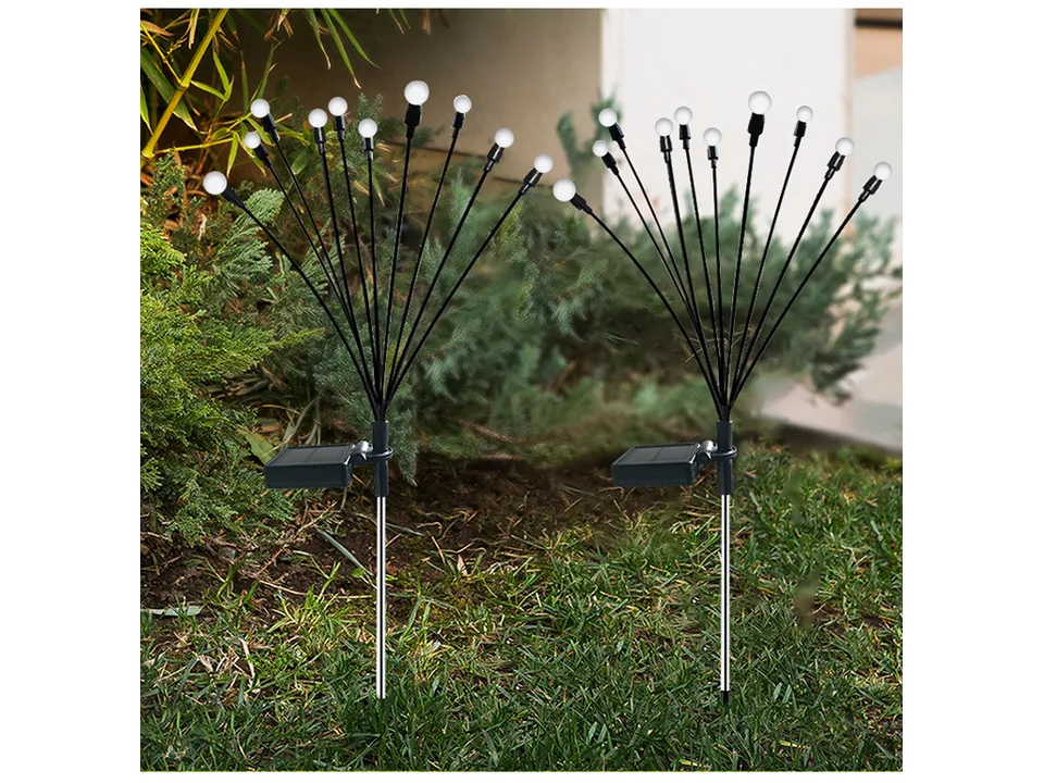 Two solar firefly garden lights standing in a garden bed during the day.