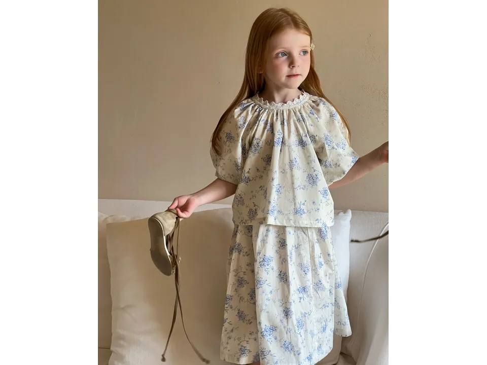 A young girl wearing a floral cotton skirt set with a lace collar.