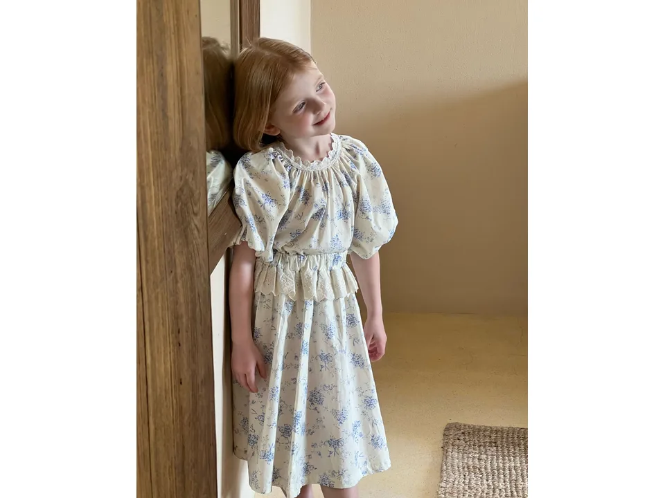 A young girl wearing a floral cotton skirt set leaning against a wall.