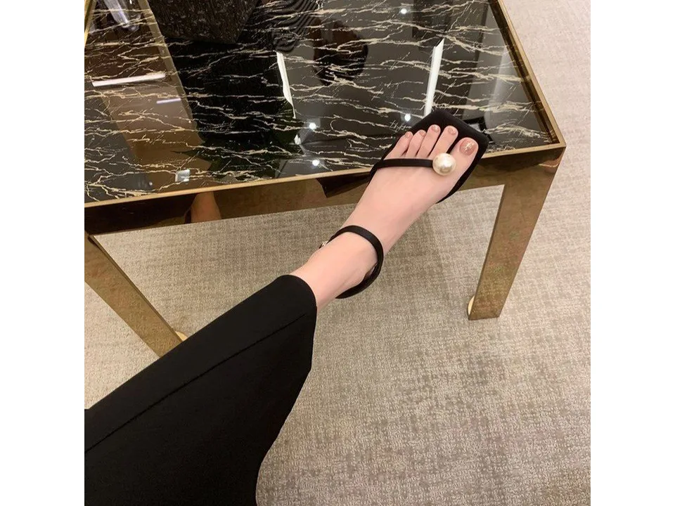 A person wearing the black pearl-embellished sandal.