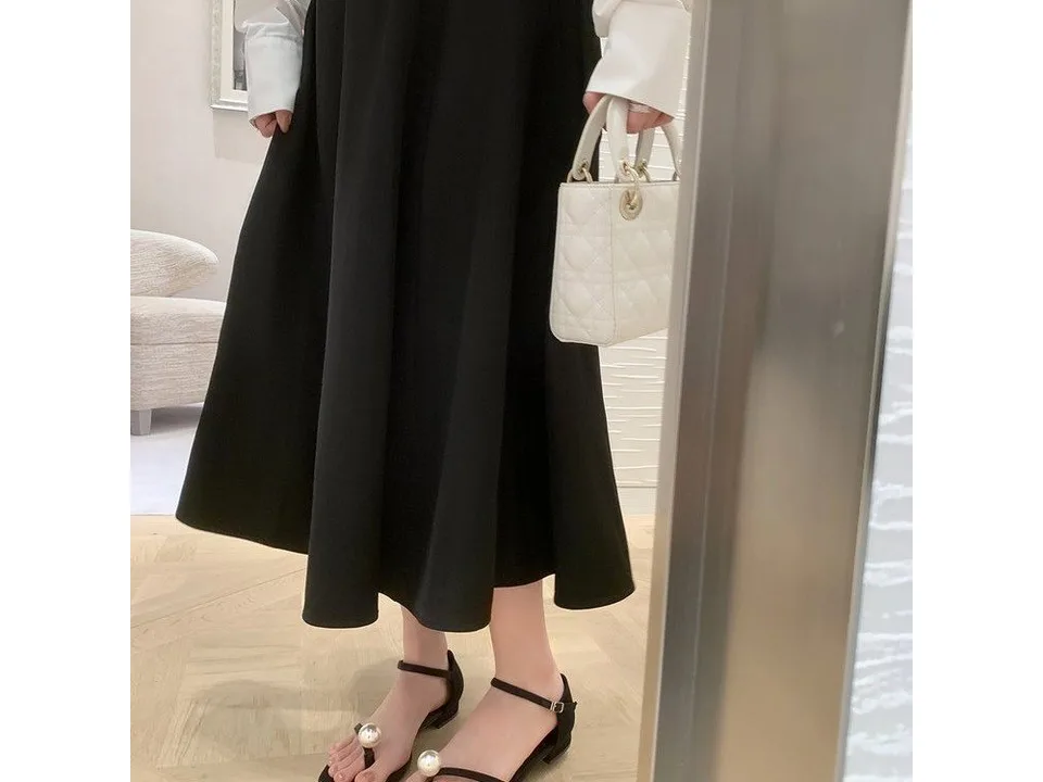 A person wearing the black sandals with a long black skirt and a white handbag.