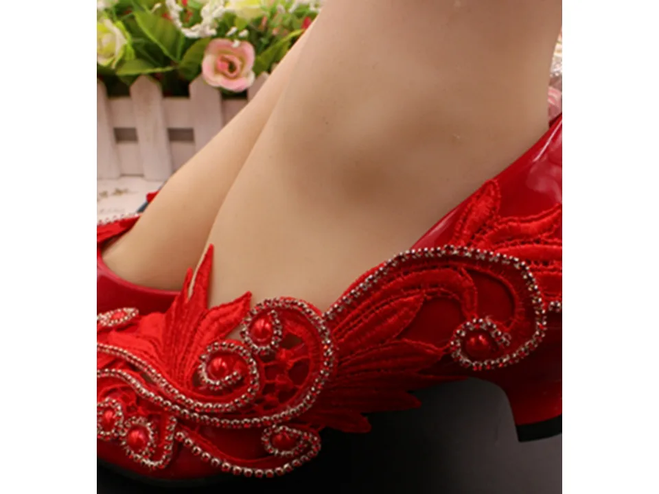 Side view of a red bridal shoe with floral lace and rhinestone details.