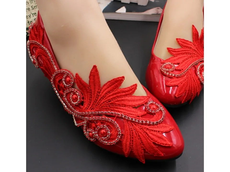 Close-up of red bridal shoes with floral lace and rhinestone embellishments on a foot.