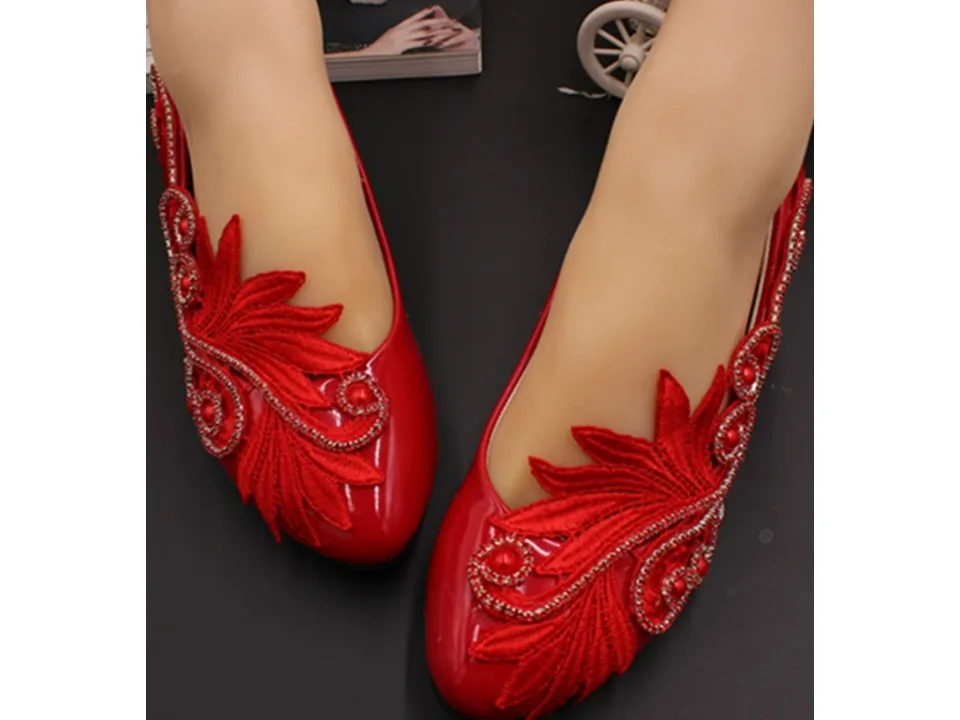 Top view of a pair of red bridal shoes with intricate lace and rhinestone detailing.