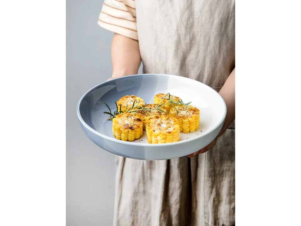 A person holding a blue and white ceramic bowl filled with corn.