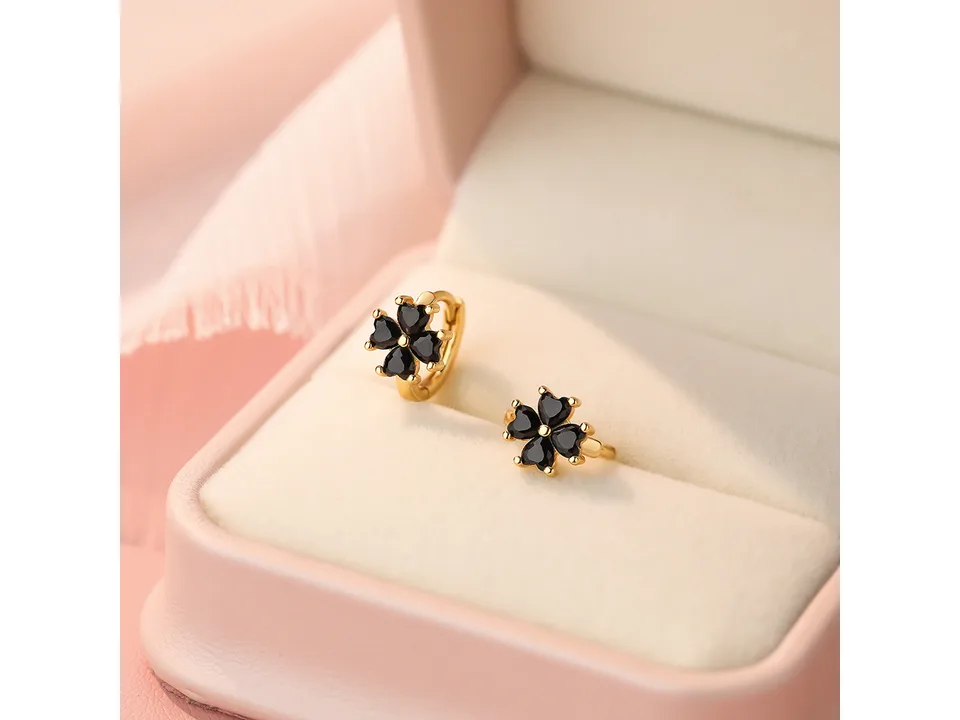 Gold clover hoop earrings with black stones displayed in a jewelry box.