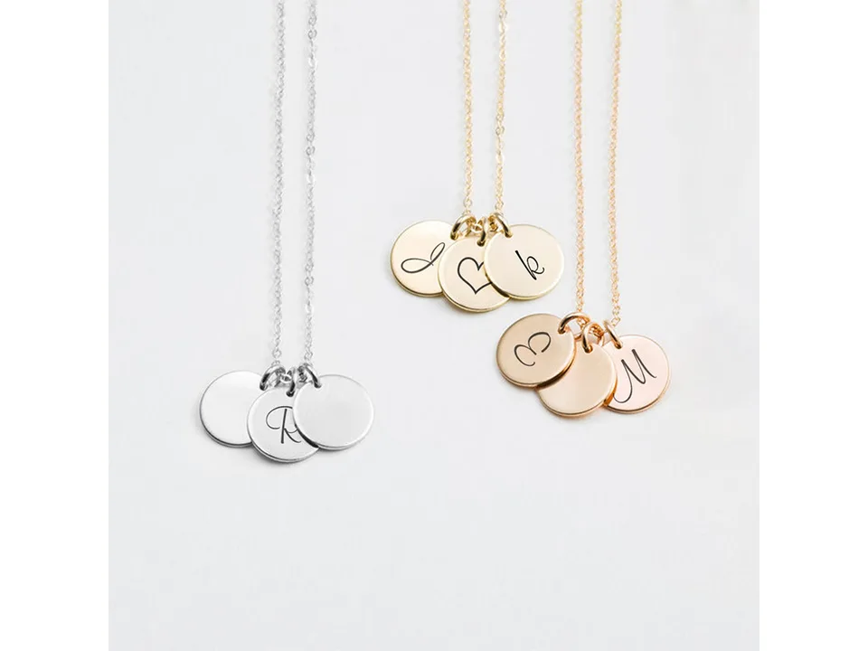 Silver, gold, and rose gold necklaces with personalized letter and heart engravings on disc pendants.