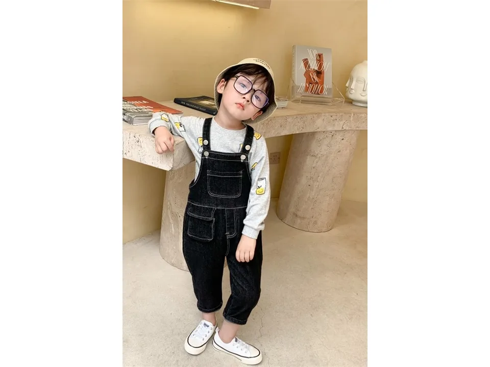 A child wearing dark denim overalls and a long-sleeved shirt.