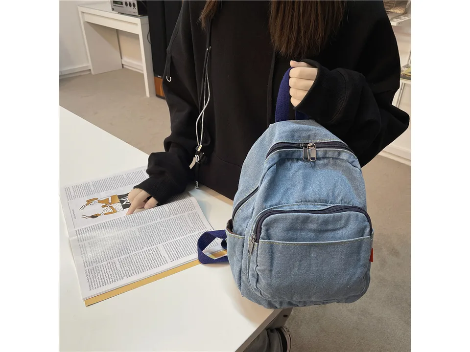 A person holding a light blue denim backpack.