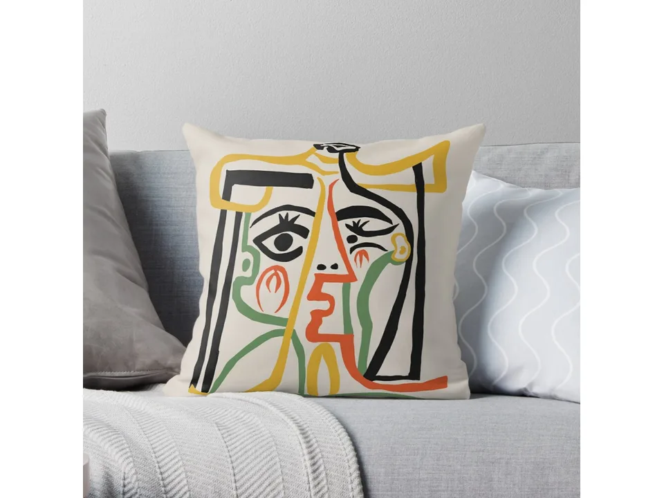 Throw pillow with a colorful abstract face design on a grey sofa.
