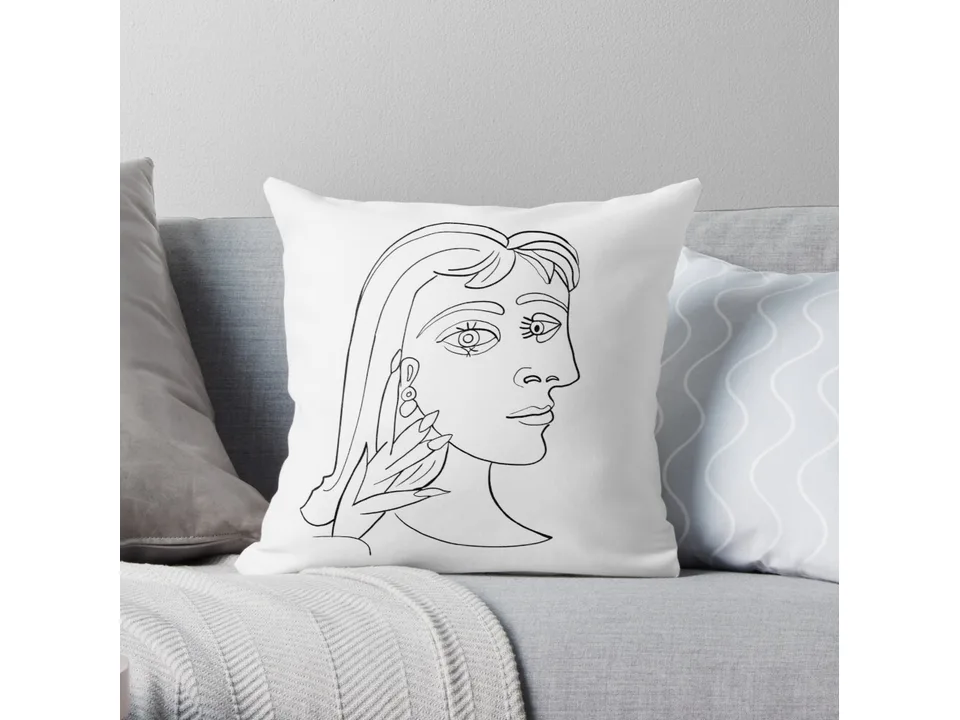 White throw pillow with a black line art portrait design on a grey sofa.