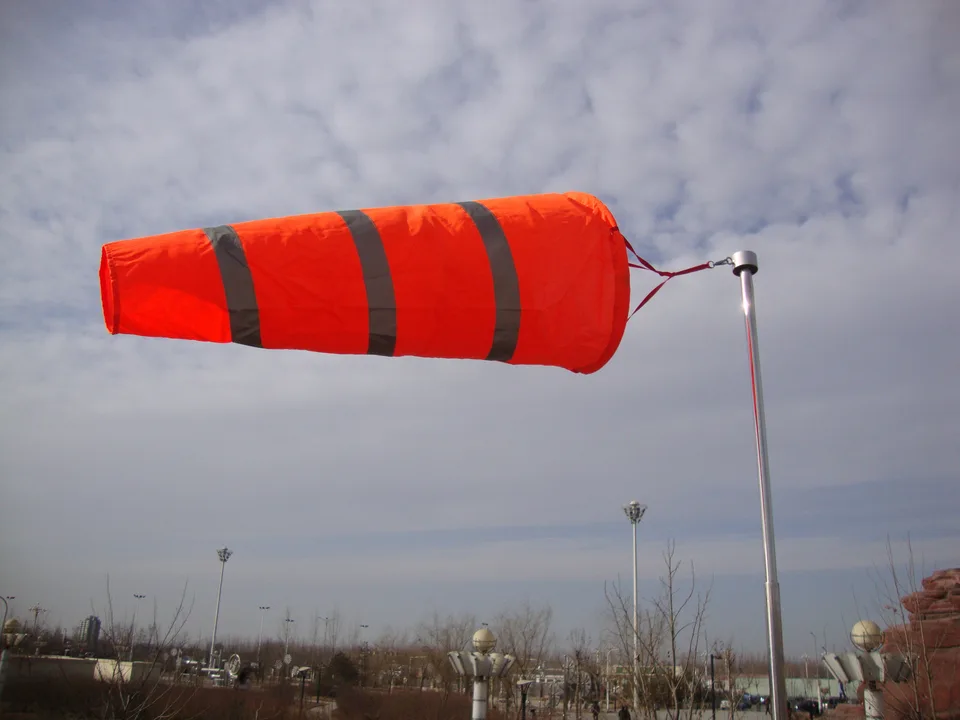 Orange windsock flying in the wind against a cloudy sky.