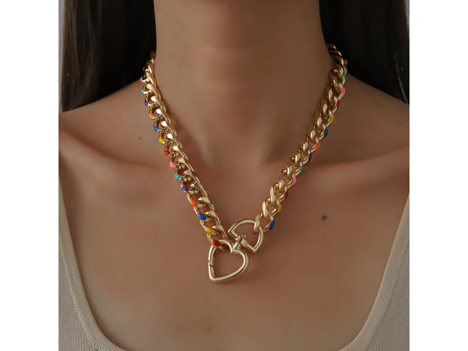 A person wearing the gold chain necklace with colorful accents and a heart pendant.