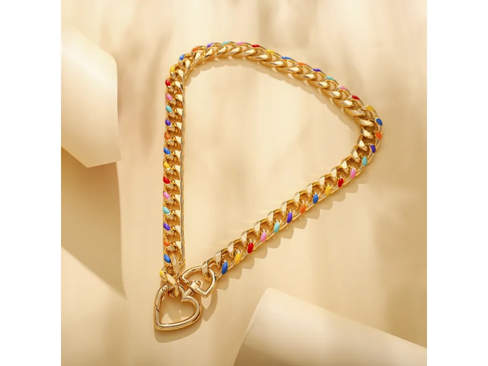 Gold chain necklace with colorful accents and a heart pendant on a beige background.