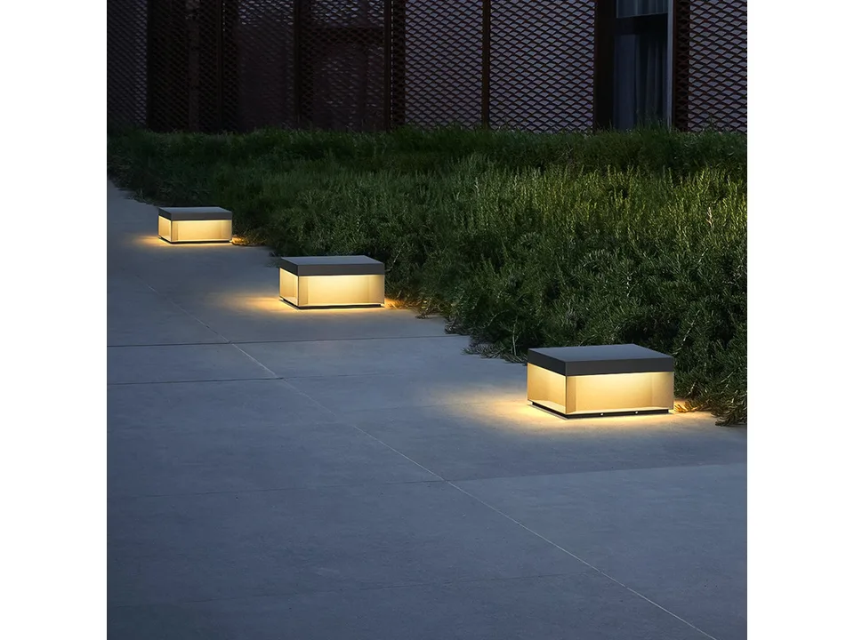 Three square solar pillar lights illuminating a concrete garden path at night.