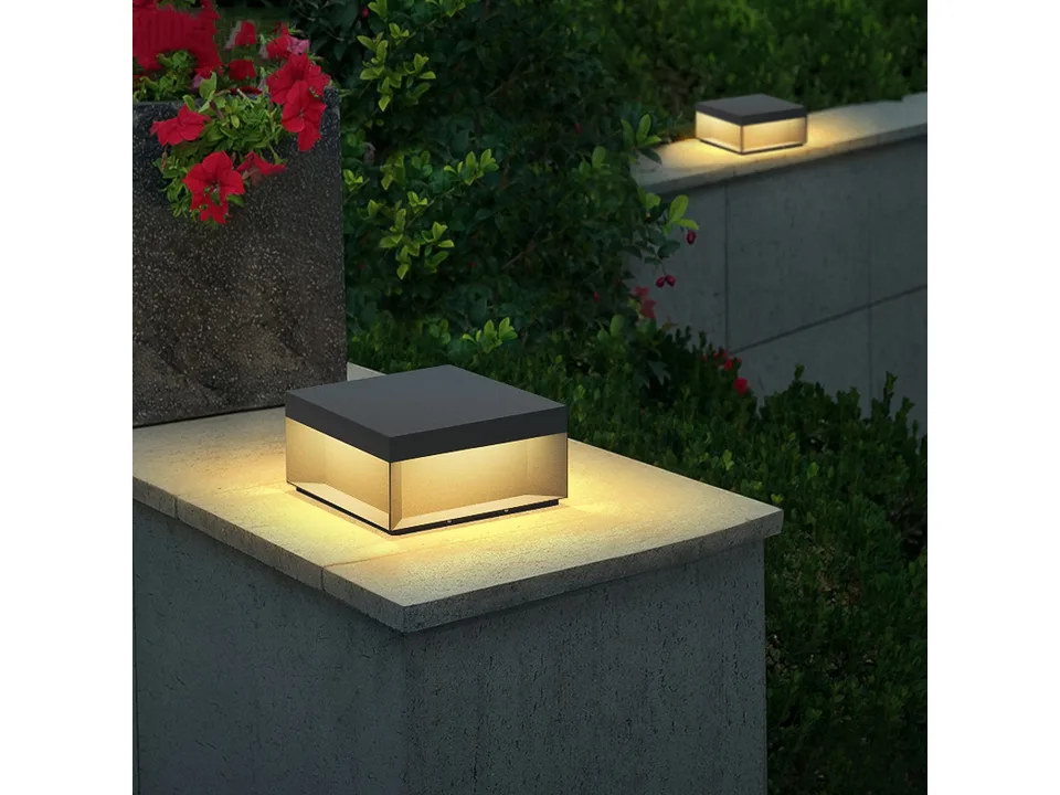 A square solar pillar light mounted on a stone wall next to a potted plant.