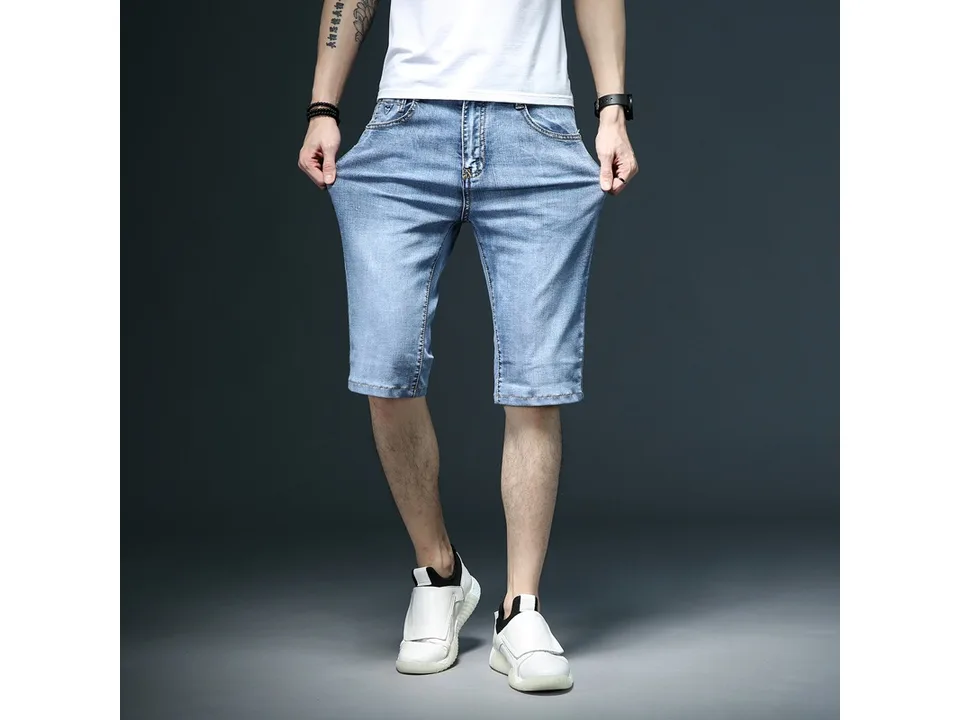 A man pulling at the waistband of blue denim shorts to show fit.
