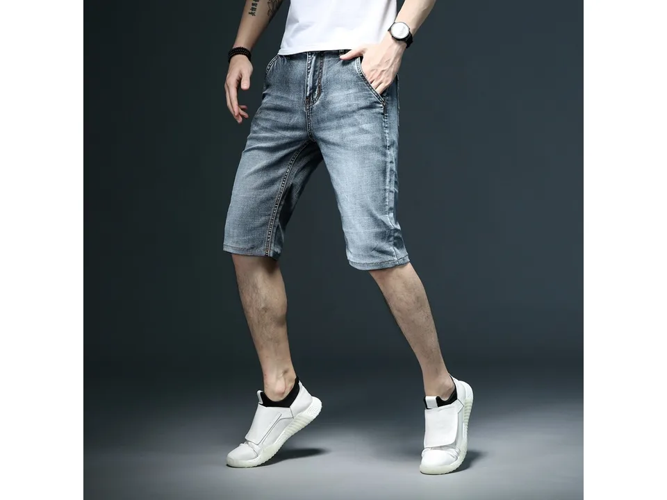 A man wearing blue denim shorts with white sneakers.