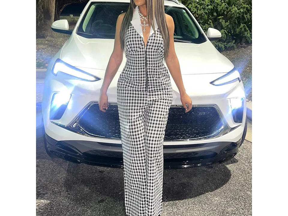 A woman standing in front of a white car wearing the black and white plaid jumpsuit.