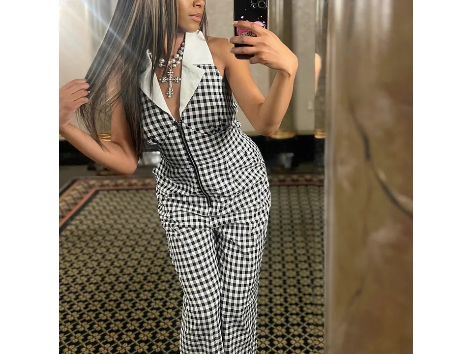 A woman wearing the black and white plaid jumpsuit, taking a mirror selfie.
