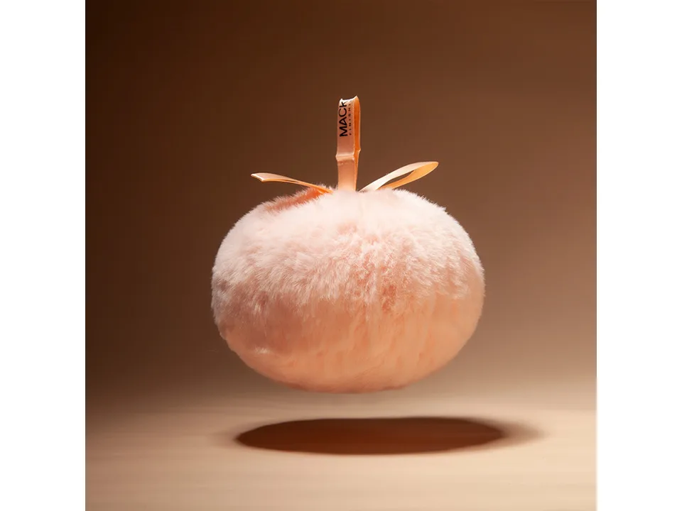 A fluffy pink makeup powder puff floating against a neutral background.