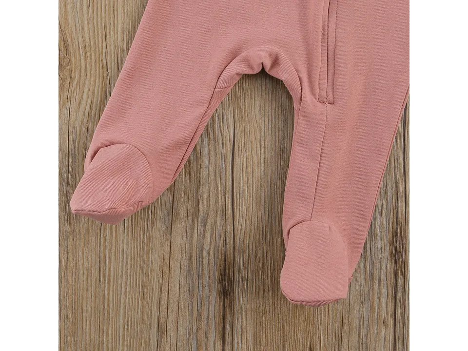 Close-up of the bottom half of a pink baby jumpsuit showing the fabric and footed feet.