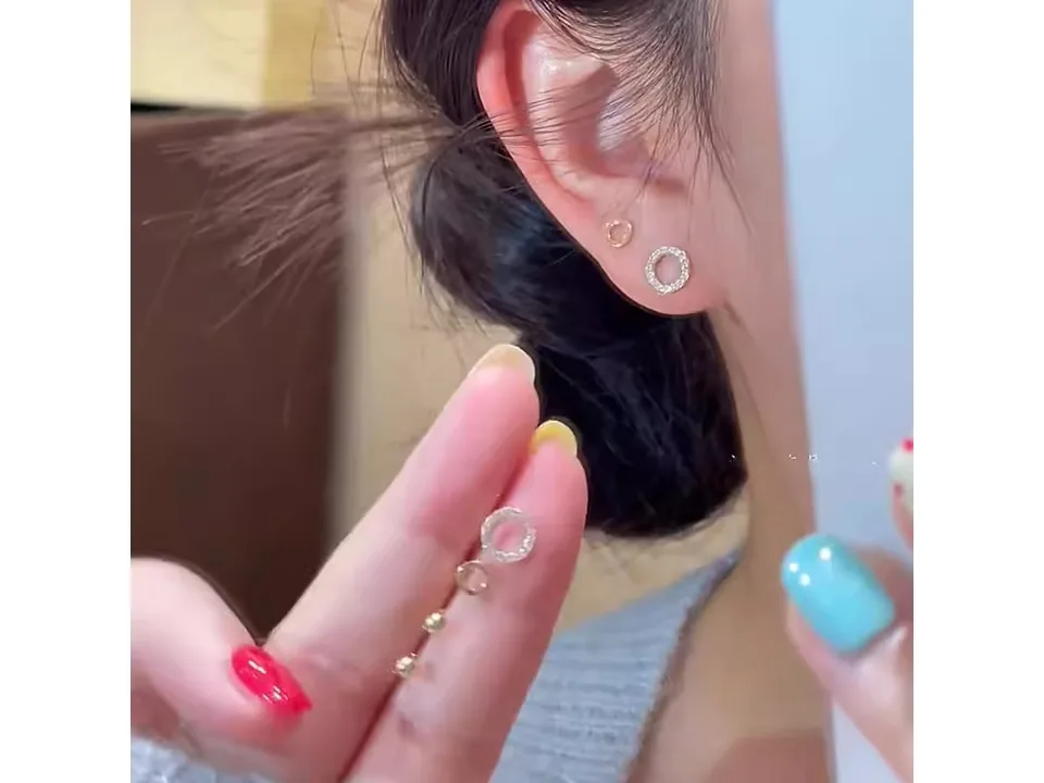 A person wearing two of the circle earrings in their earlobe.