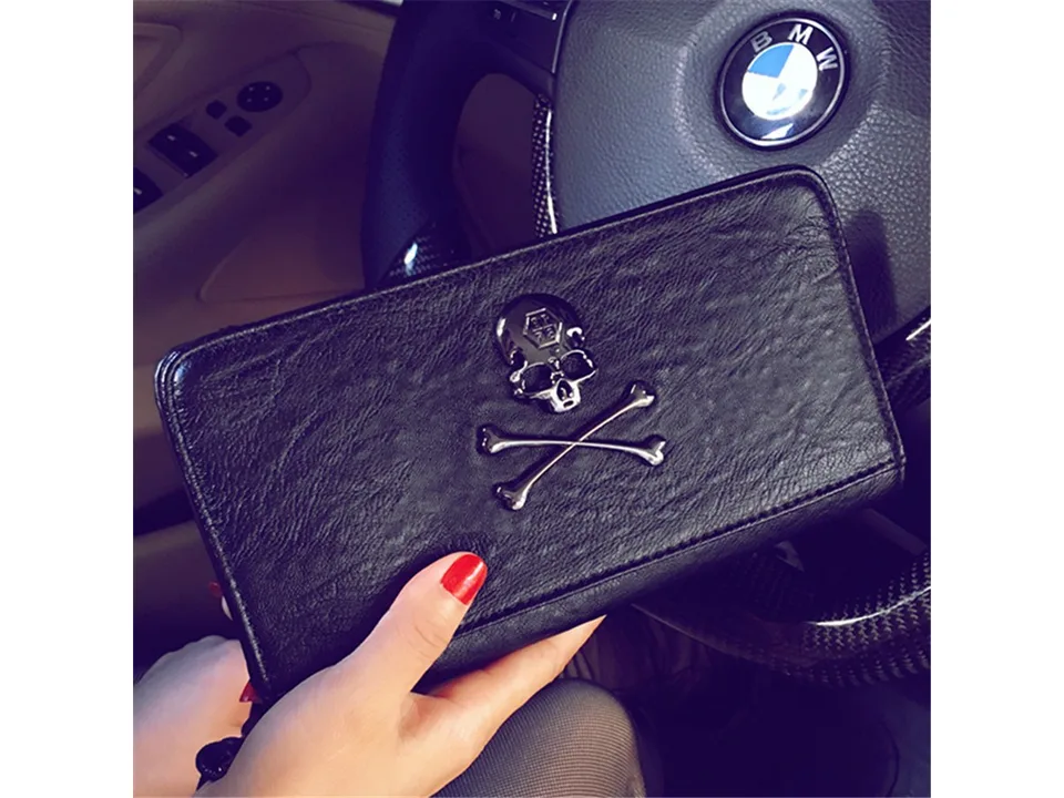 Black skull motif zip-around wallet held in a hand inside a car.