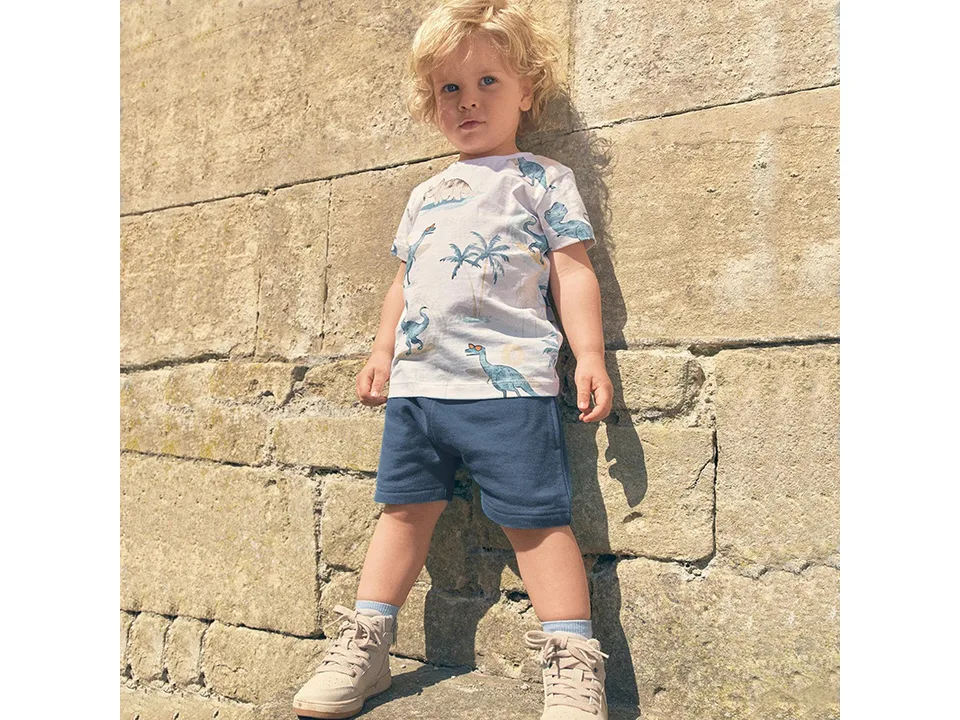 A young boy wearing the dinosaur print t-shirt and blue shorts outfit