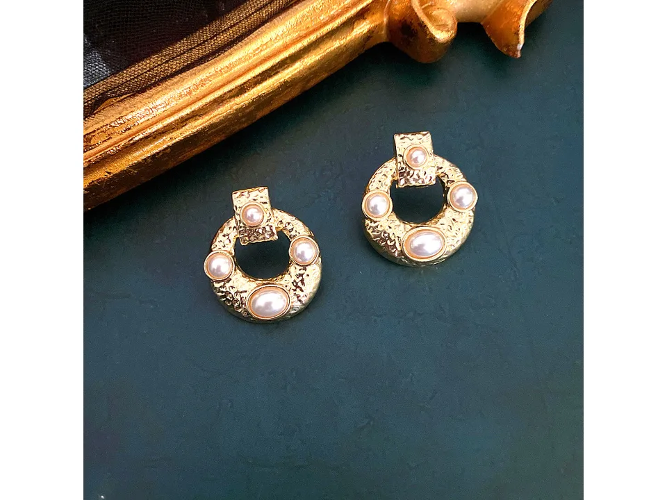 The gold and pearl hoop earrings resting on a dark surface next to a gold frame.