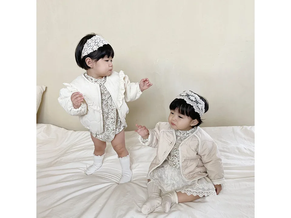 Two babies wearing the cream quilted jacket with ruffle details.