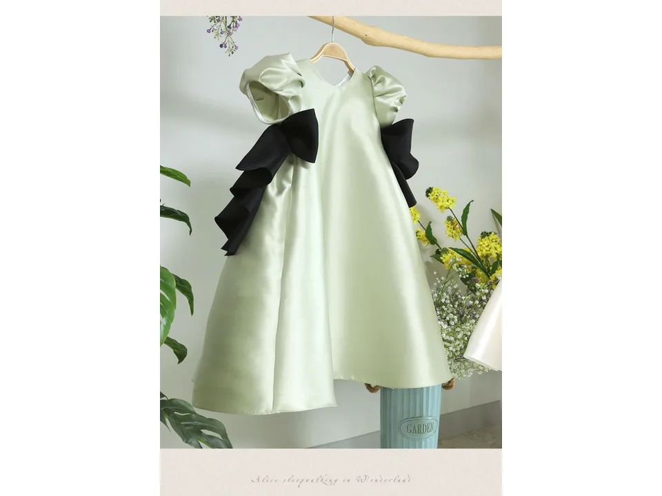 A light green puff-sleeve dress with black bows hanging on a wooden hanger.