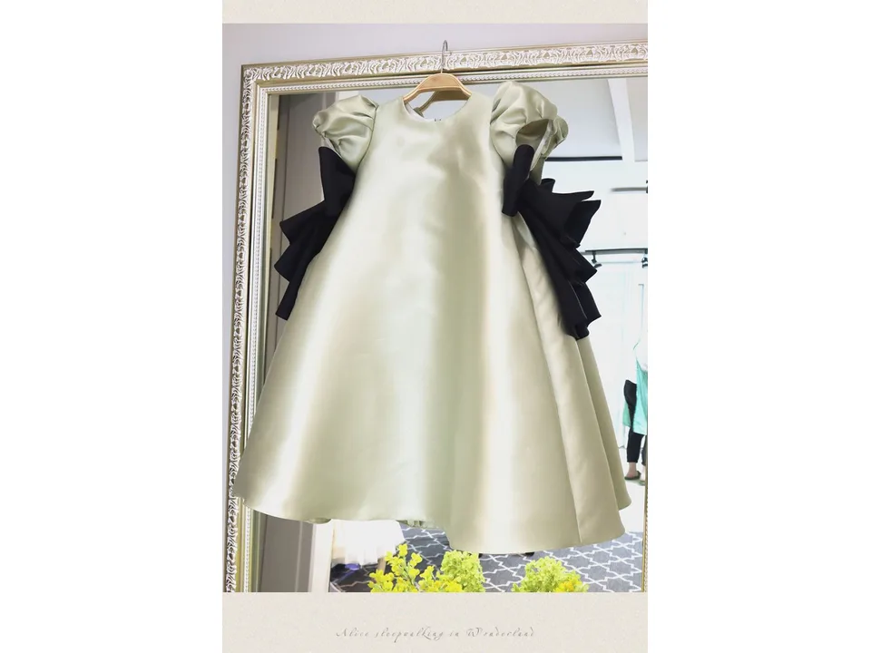 A light green puff-sleeve dress with black bows hanging in front of a mirror.