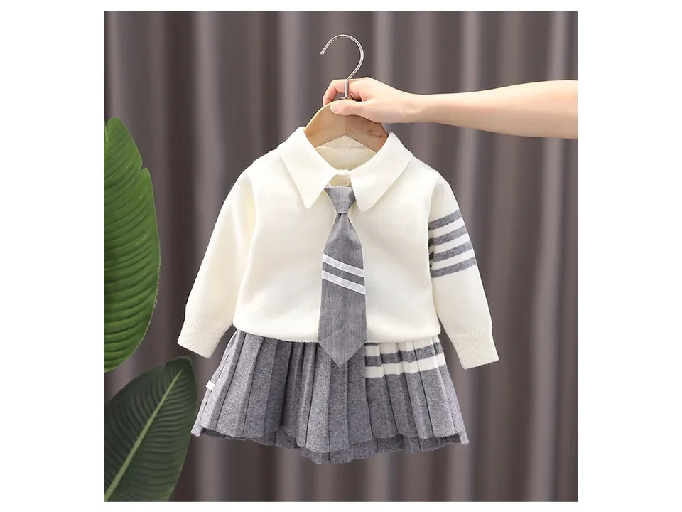 A girls knitted sweater and pleated skirt set with a tie, hanging on a hanger.