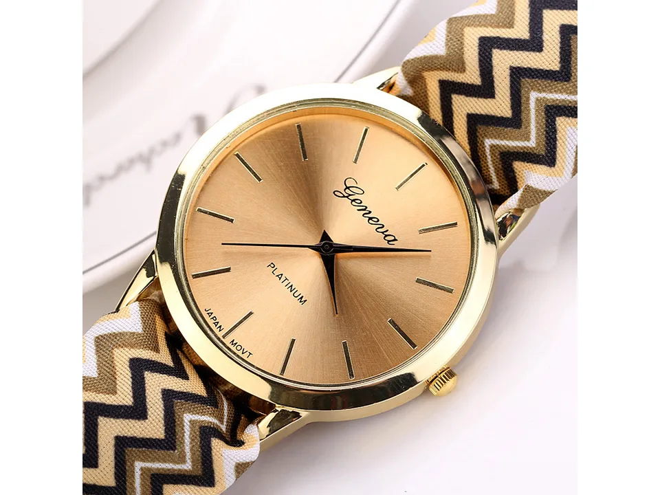Close-up of a gold-faced watch with a brown, black, and white chevron fabric strap.