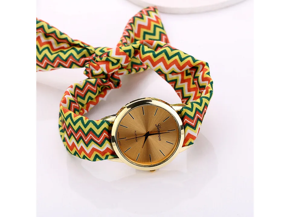 A woman wearing a gold-faced watch with a green, orange, and yellow chevron fabric strap on her wrist.