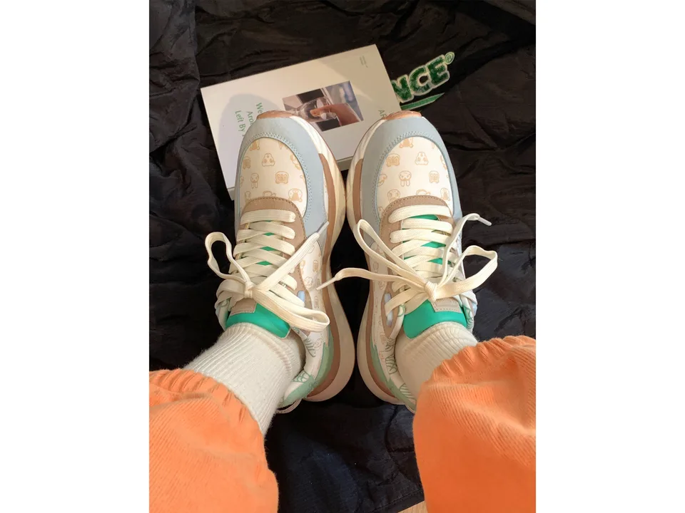 A pair of cute low-top sneakers with a macaron color scheme worn on feet.