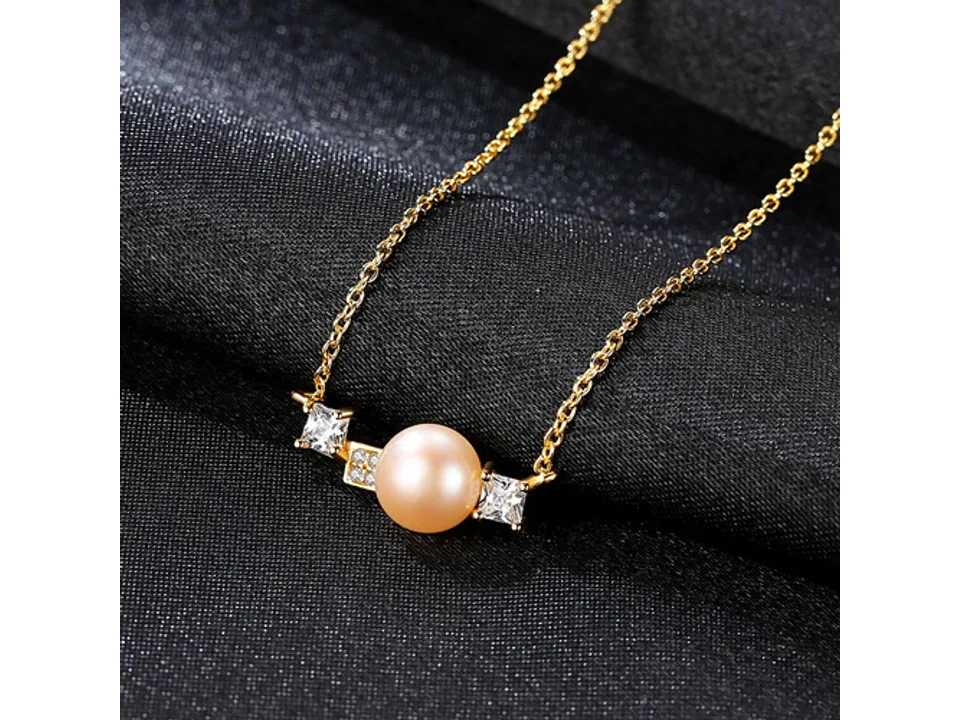 Close-up of a gold necklace with a pearl and geometric crystal accents on a black fabric background.