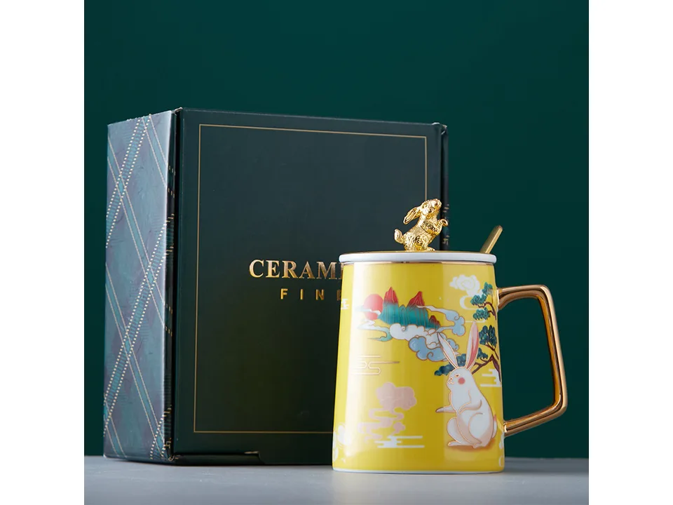 Yellow ceramic rabbit mug with lid and spoon next to its gift box.