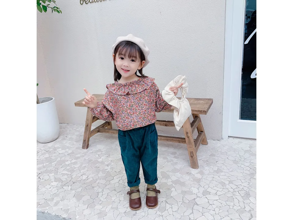 A young girl wearing a floral long-sleeve blouse and dark green trousers.