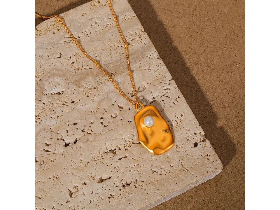 Gold pearl pendant necklace resting on a textured stone surface.