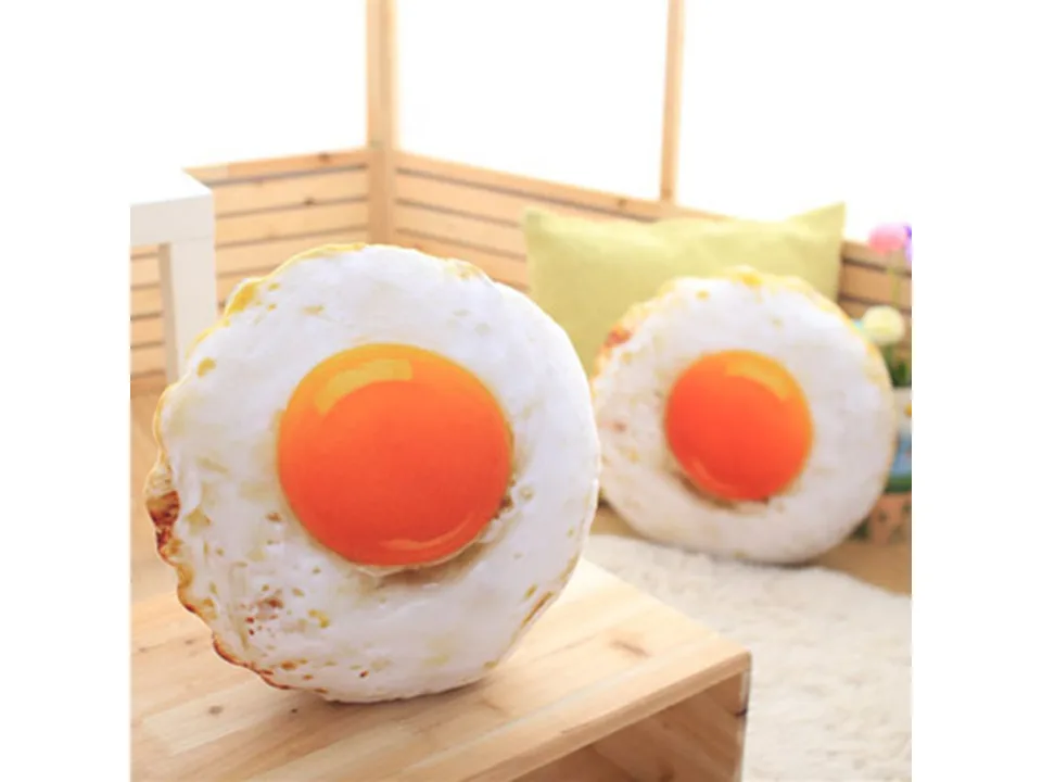 Two fried egg shaped plush pillows on a wooden table.