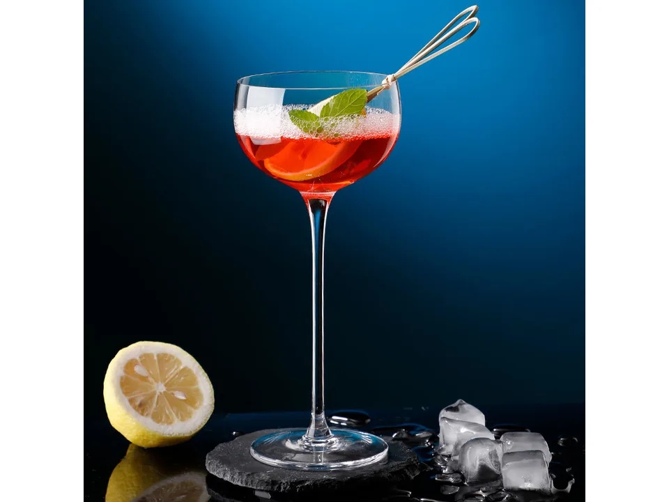 A stemmed cocktail glass filled with a red drink, garnished with a lemon slice and mint.