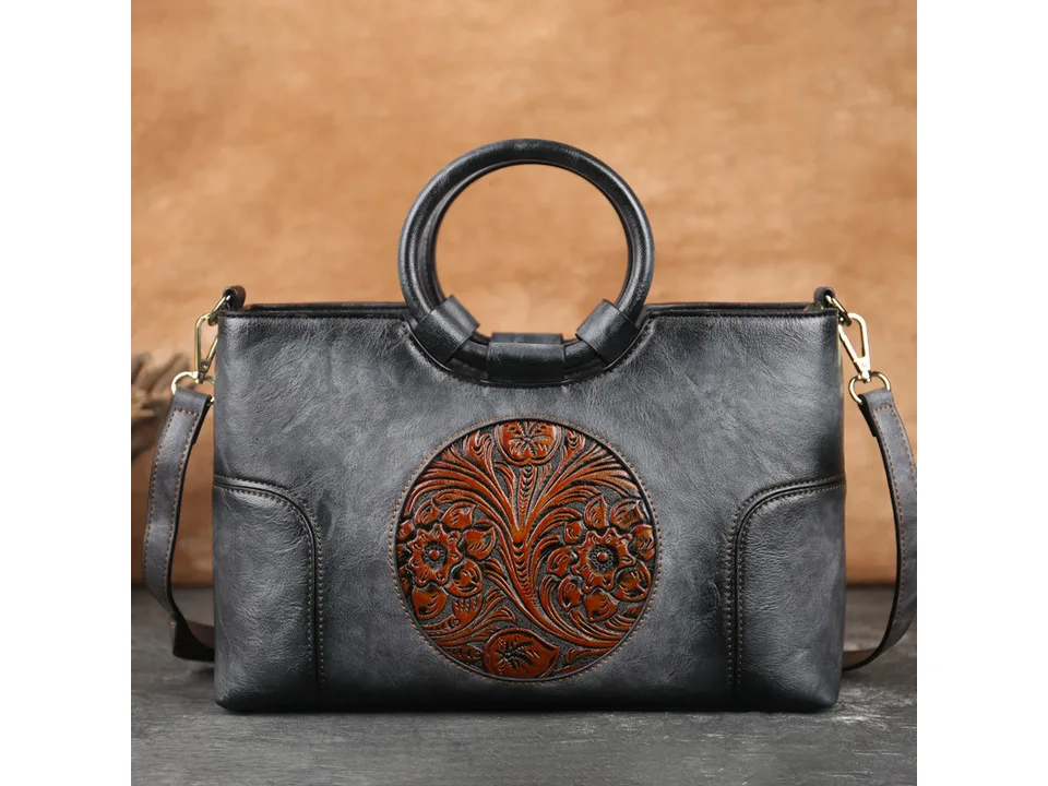 Black vintage-style handbag with a round handle and floral embossed circular design.