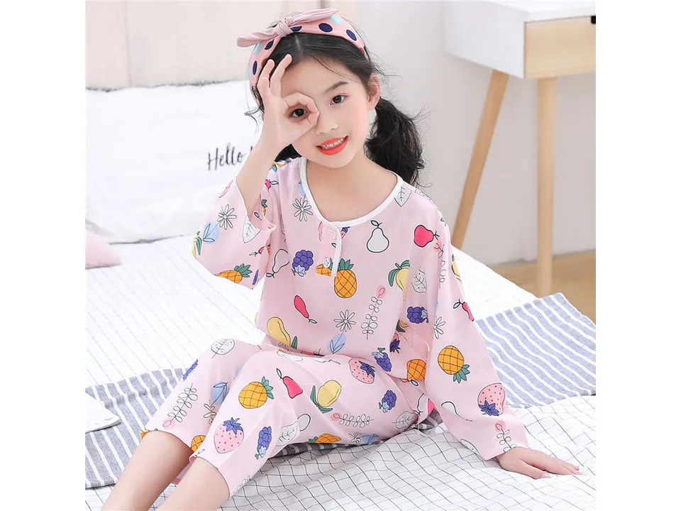 A young girl wearing a pink long-sleeve pajama set with a fruit print and a matching headband.